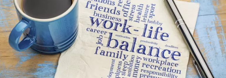 Coffee cup and pen on a table with a napkin featuring a word cloud about work-life balance.