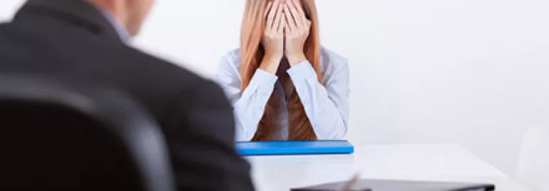 Woman sitting at a table with her head in her hands, looking stressed.