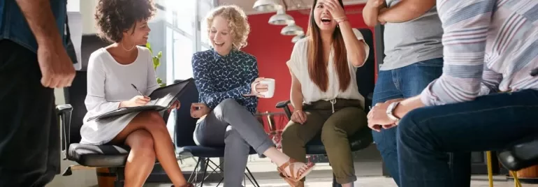 Group of colleagues laughing and chatting in an office setting.