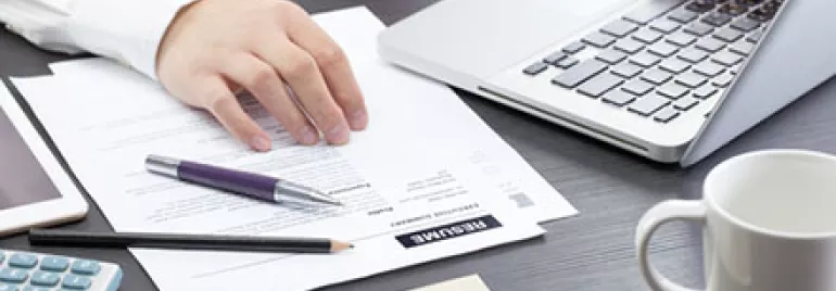 Person working on a laptop with documents, a calculator, and glasses on a desk.