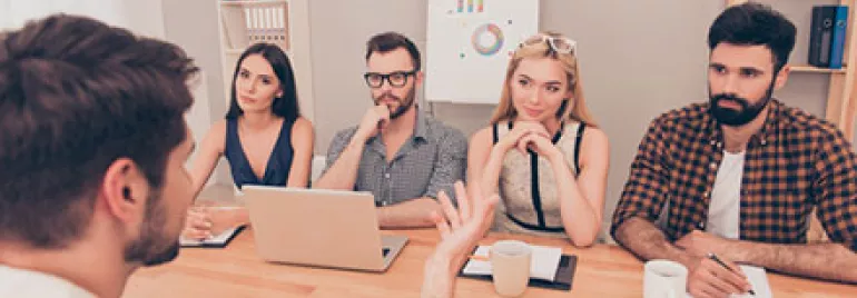 Group interview with four people listening to a speaker at a table.