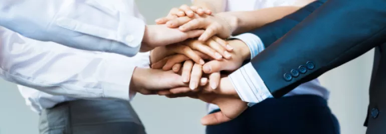 Group of people placing hands together in a teamwork gesture.
