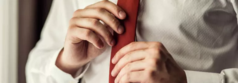 Person adjusting a red tie while wearing a white shirt.