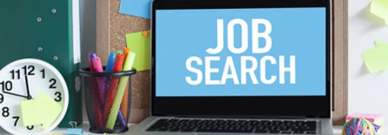 Laptop screen with 'Job Search' text surrounded by office supplies.