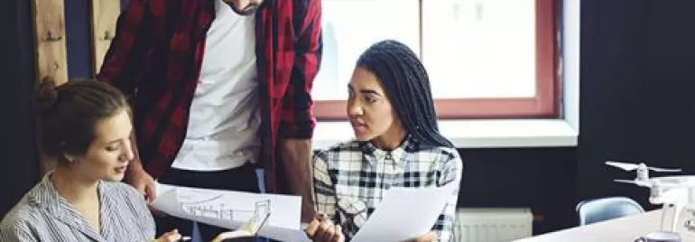 Three people discussing architectural plans at a table.