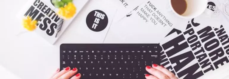 Hands typing on a keyboard with motivational posters and a coffee cup on a white table.