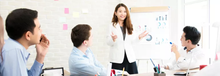 Team meeting with a woman presenting data on a flip chart.