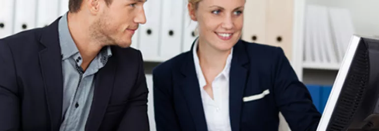 Two colleagues in suits working at a computer in an office.