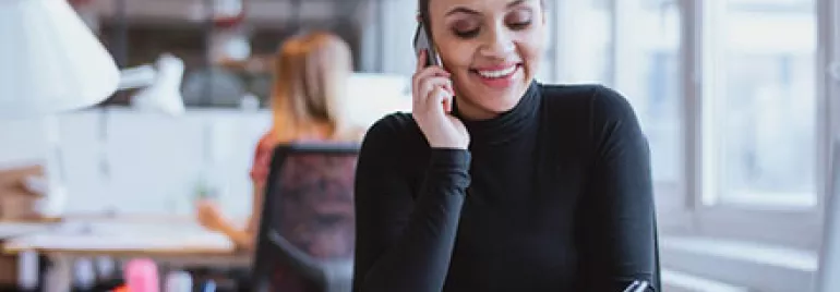 Woman in office talking on phone and taking notes.