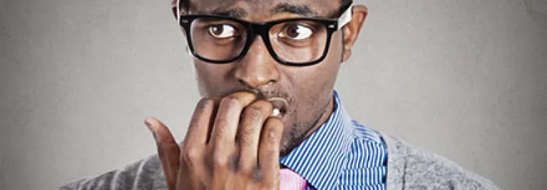 Man with glasses biting nails, looking worried.