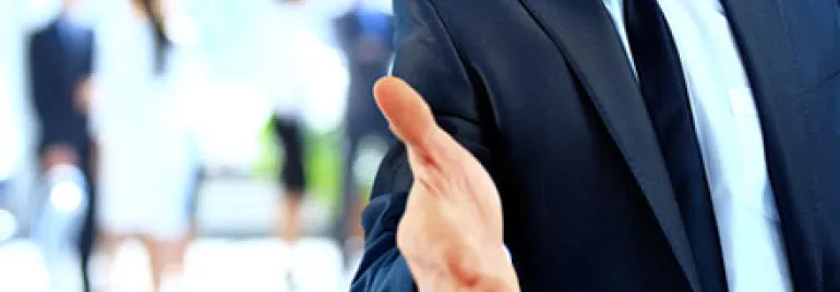 Businessman in a suit reaching out for a handshake.