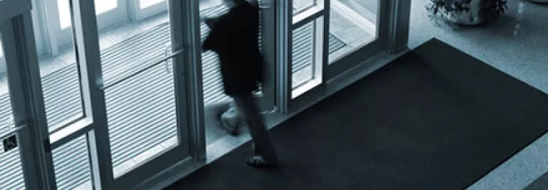 Blurred silhouette of a person exiting through glass doors.