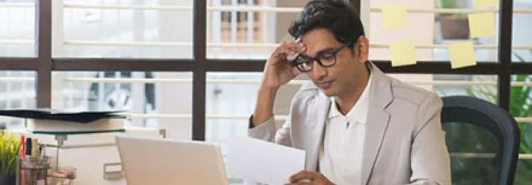 Man at desk reading paper by laptop with post-it notes on the window.