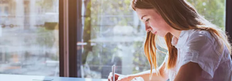 Woman writing at a sunlit desk.