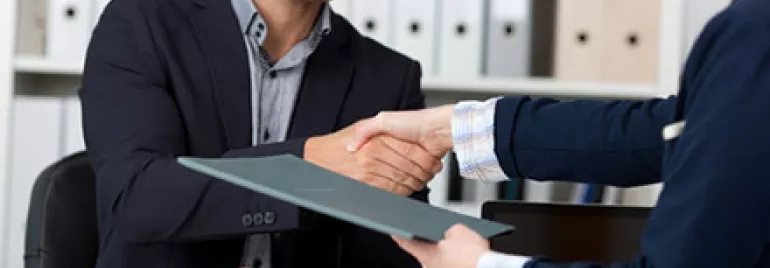 Two people shaking hands over a desk in an office.