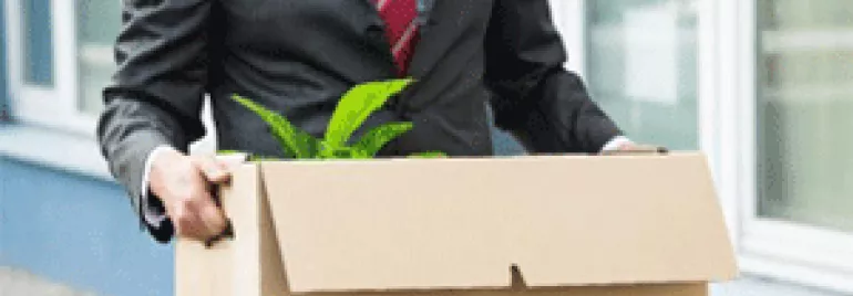 Businessman in a suit carrying a cardboard box with a plant.