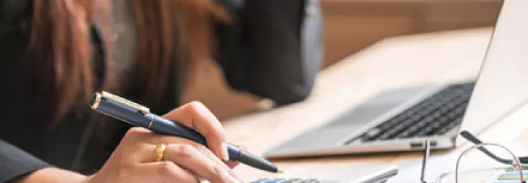 Person using a calculator at a desk with a laptop and papers.