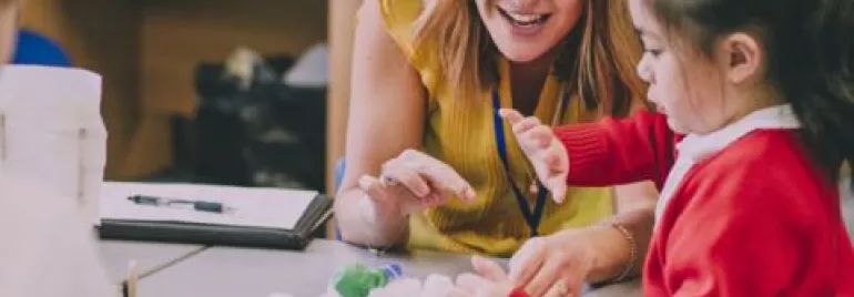 Teacher assisting a child with a toy car in a classroom setting.