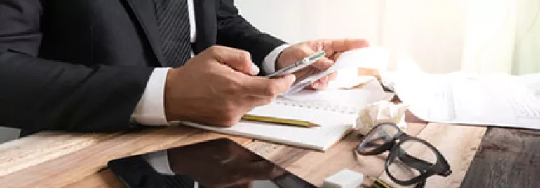 Businessman using smartphone at desk with glasses and tablet.