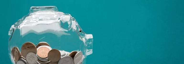 Clear piggy bank filled with various coins against a teal background.