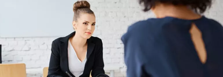 Two women in a professional interview setting, one writing notes.
