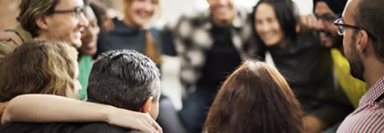 A diverse group of people sitting closely in a circle, smiling and embracing each other.