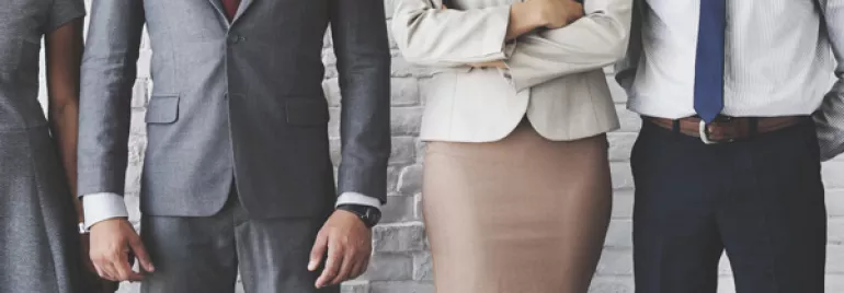 Group of professionals in business attire standing in front of a white brick wall.