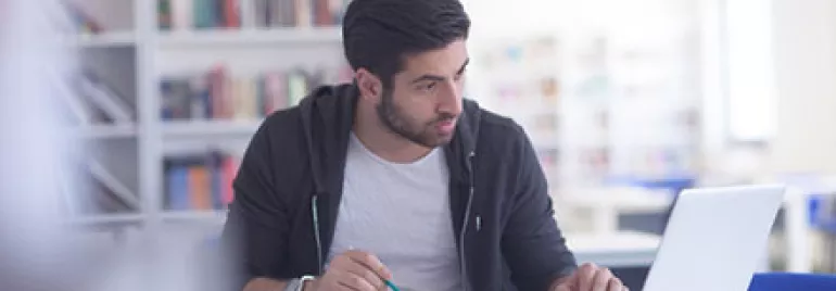Man studying with a laptop and book in a library.