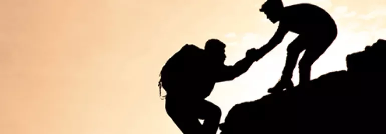 Silhouette of two climbers helping each other on a rocky cliff.