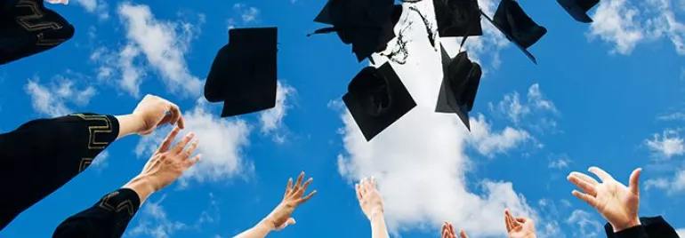 Graduates throwing caps in the air against a blue sky with clouds.