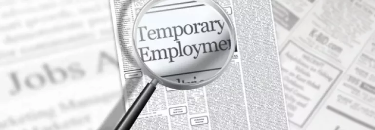 Magnifying glass over newspaper classifieds highlighting 'Temporary Employment'.