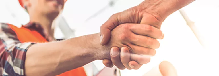 Construction worker in orange vest shaking hands with another person.