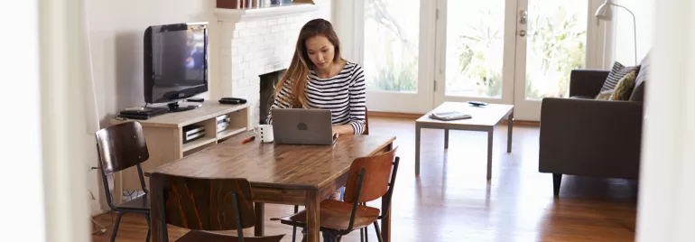 Person working on a laptop at a dining table in a cozy living room.