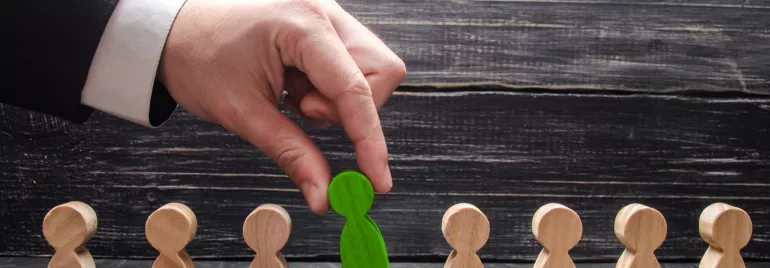 Hand selecting a green wooden figure from a row of plain wooden figures.