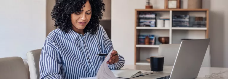 Person working at a table with documents and a laptop.