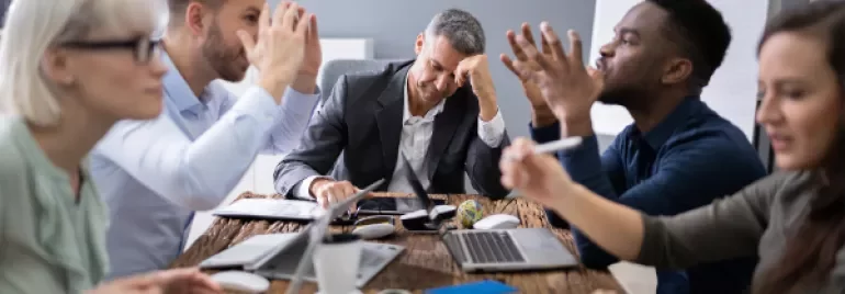 Group of people having a lively discussion in a meeting room with laptops on the table.