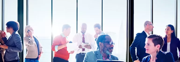 Colleagues mingling and discussing in a modern office with large windows.