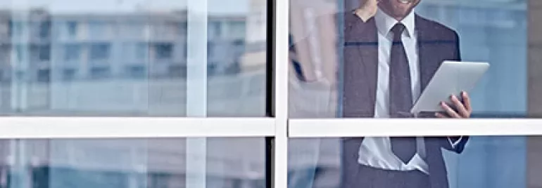 Businessman talking on phone and using a tablet by a window.