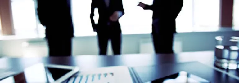 Three businesspeople discussing in an office with documents and charts on the table.