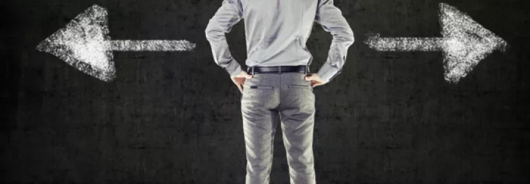 Back view of man facing two chalk-drawn arrows on a blackboard, one pointing left and the other right.