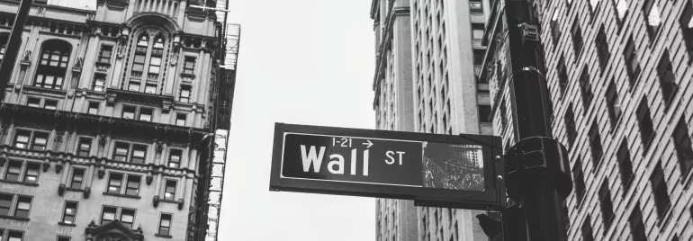 Black and white photo of Wall Street sign with tall buildings in the background.
