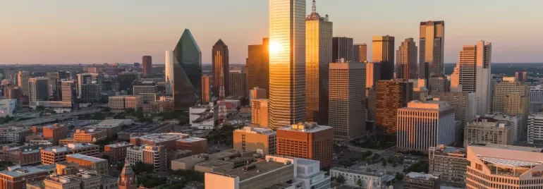 Aerial view of a city skyline at sunset, with skyscrapers reflecting golden light.