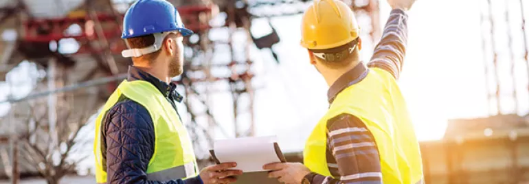 Two construction workers in safety gear discussing a building site.