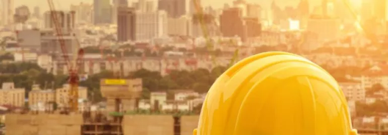 Yellow construction helmet and gloves on a ledge, city skyline in the background.
