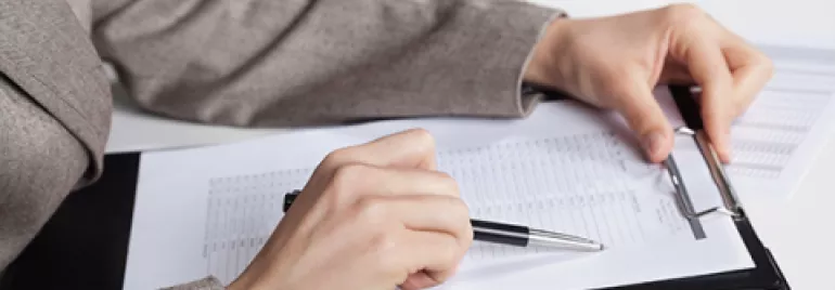 Person in suit reviewing documents on clipboard at desk.