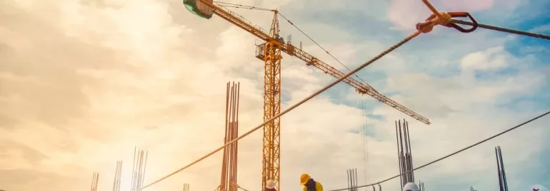 Construction workers on a building site with cranes and scaffolding under a bright sky