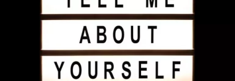Lit sign displaying the phrase 'Tell me about yourself.'