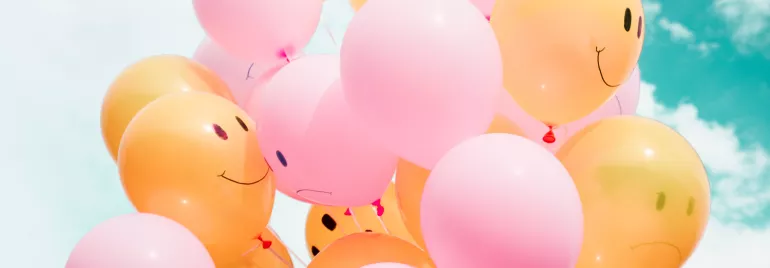 Pink and yellow balloons with smiley faces floating in the sky.