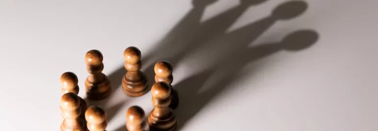 Chess pawns casting the shadow of a king.