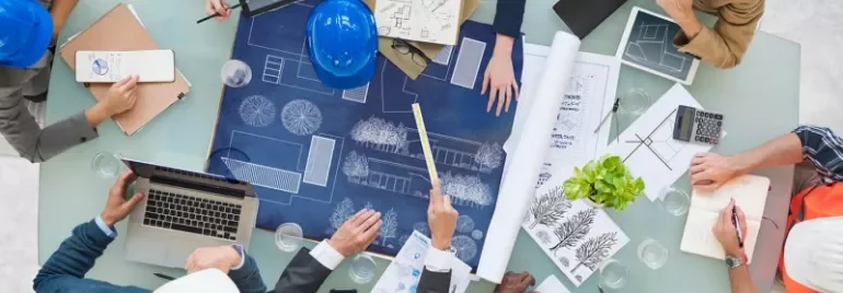 People collaborating over architectural blueprints at a table.